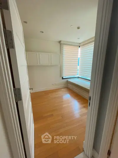 Bright bedroom with wooden floors and large windows with blinds.