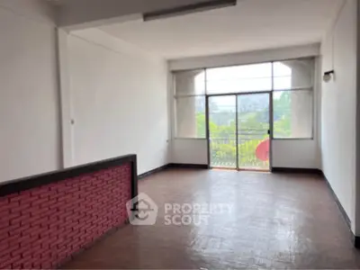 Spacious living room with large windows and balcony access, offering abundant natural light and greenery views.