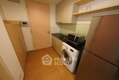 Compact kitchen with modern appliances including washing machine and microwave, sleek cabinetry, and wooden flooring.