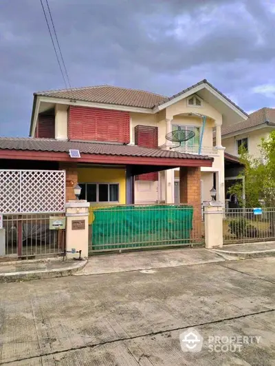 Charming two-story residence with red shutters and a cozy balcony, featuring a secure gated entrance and a quaint front porch, nestled in a peaceful neighborhood.