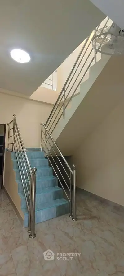 Modern staircase with sleek metal railings and tiled steps in a well-lit interior space.