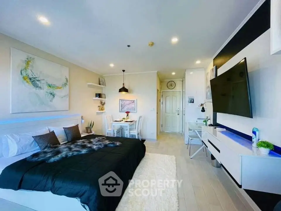 Modern studio apartment with stylish decor and cozy ambiance, featuring a large bed, dining area, and wall-mounted TV.