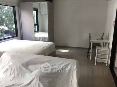 Spacious bedroom with two beds, large windows, and a study desk, offering natural light and modern decor.
