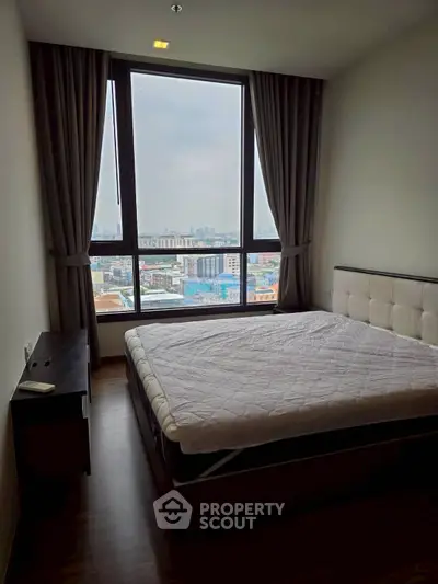 Modern bedroom with large window offering city view, featuring a comfortable bed and elegant curtains.