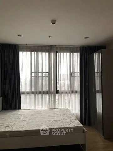 Spacious bedroom with large windows and modern furnishings in a high-rise apartment.