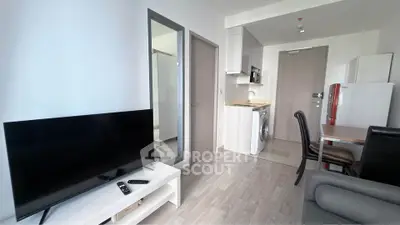 Modern living room with TV, washing machine, and sleek kitchen area in a compact apartment.