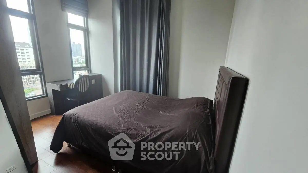 Cozy bedroom with large windows and a city view, featuring a comfortable bed and a study desk.