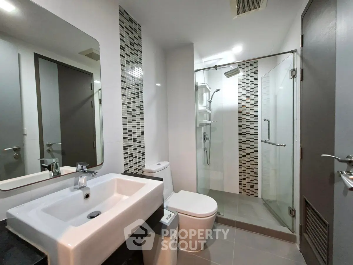 Modern bathroom with glass shower and sleek fixtures in contemporary apartment.