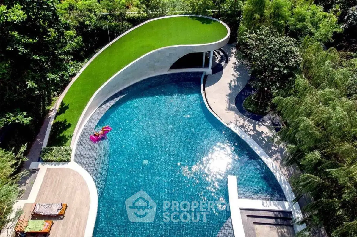 Luxurious curved swimming pool surrounded by lush greenery, perfect for relaxation and leisure.