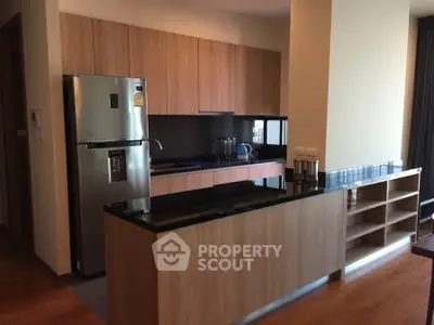 Modern kitchen with sleek wooden cabinets and stainless steel fridge in open layout design.