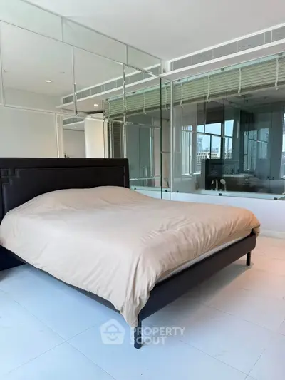 Spacious modern bedroom with mirrored walls and city view, featuring a sleek bed and minimalist design.