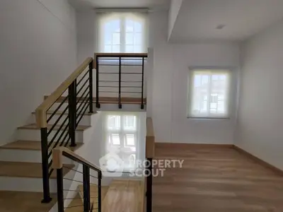 Modern staircase with wooden flooring and large windows in a bright interior space.