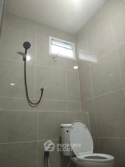 Modern bathroom with sleek tiles and showerhead, featuring a compact design.