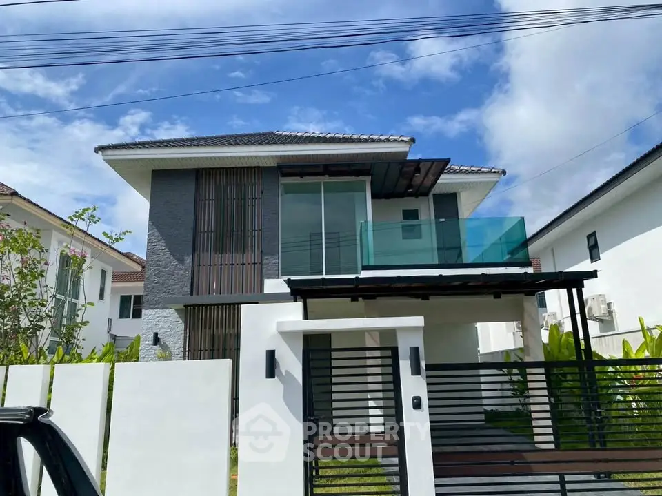 Modern two-story house with sleek design and glass balcony under a clear blue sky.