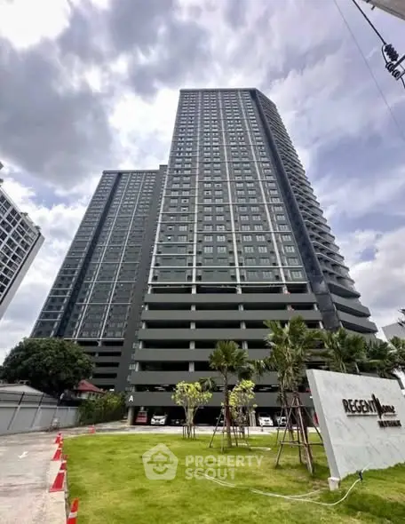 Modern high-rise condominium with lush green landscaping and clear sky view.