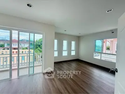 Spacious living room with large windows and balcony access, offering abundant natural light and a modern wood floor.