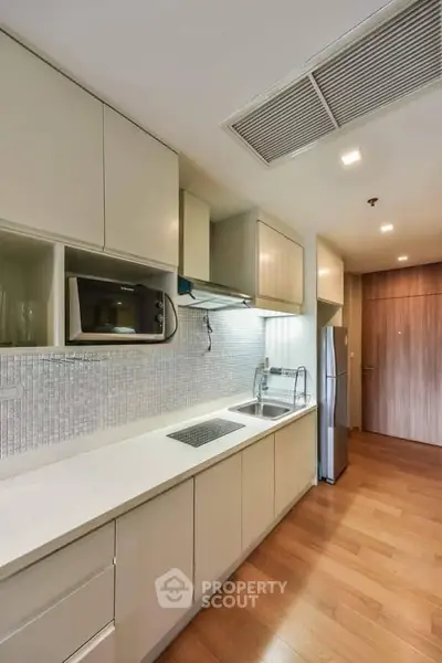Modern kitchen with sleek cabinetry, built-in microwave, and stainless steel fridge in a stylish apartment.