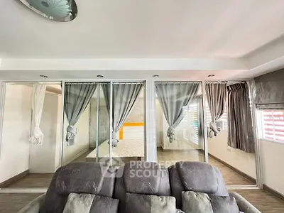 Spacious living room with modern decor and glass partitions leading to a cozy bedroom.