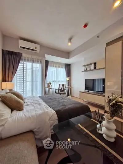 Modern bedroom with stylish decor and natural light, featuring a cozy bed and a sleek TV unit.