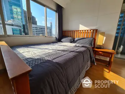 Spacious bedroom with large windows offering ample natural light and a stunning city view, featuring a comfortable bed and polished wooden furniture.