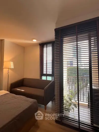 Cozy bedroom with a small balcony and modern decor, featuring a comfortable sofa and stylish blinds.