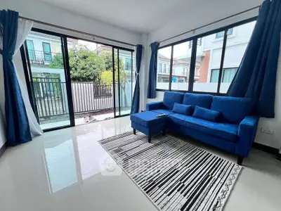 Bright living room with blue sofa and large windows overlooking garden view.