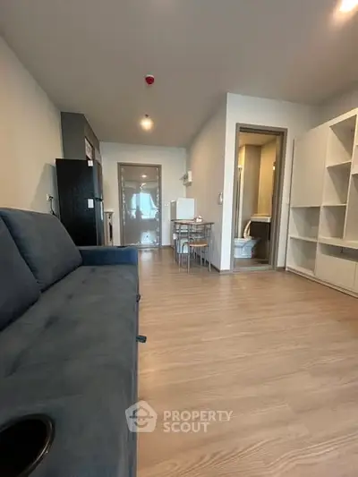 Modern living room with sleek furniture and open layout, featuring a cozy blue sofa and dining area.