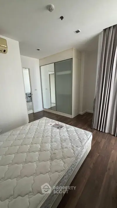 Spacious bedroom with hardwood floors and large mirrored closet in modern apartment.