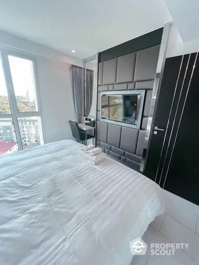 Modern bedroom with sleek design and city view, featuring a wall-mounted TV and cozy workspace.