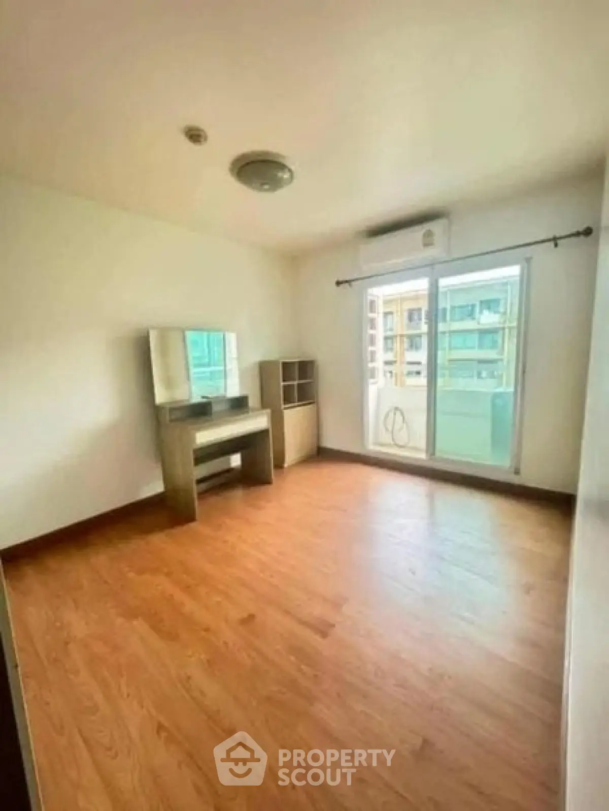 Spacious empty bedroom with wooden flooring and large window in modern apartment.