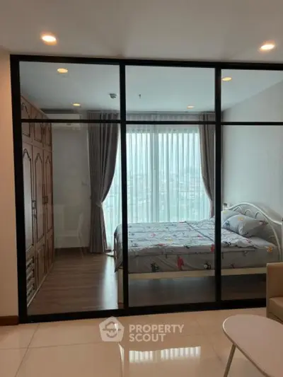 Modern bedroom with glass partition and city view, featuring stylish decor and ample natural light.