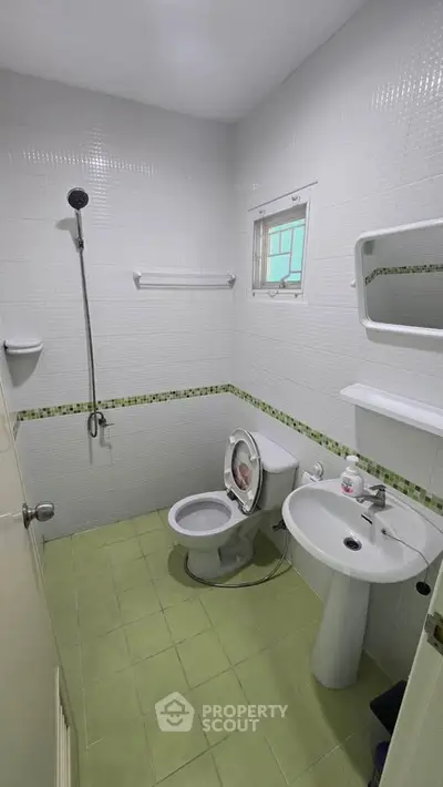 Compact bathroom with green tile flooring, shower, toilet, and sink in a modern apartment.