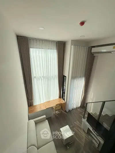 Modern loft-style living room with high ceilings and large windows, featuring sleek furniture and abundant natural light.