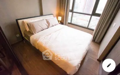 Cozy bedroom with large window offering city views, featuring a comfortable bed and warm lighting.