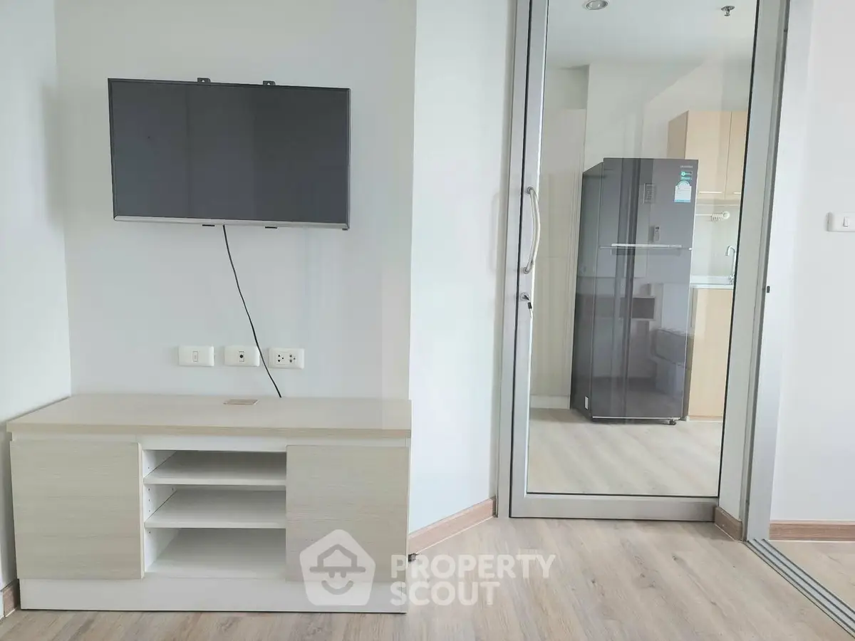 Modern living room with wall-mounted TV and sleek storage unit, adjacent to a glass door leading to a kitchen.