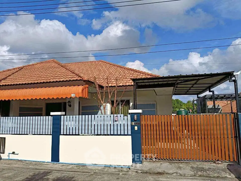 Charming single-story house with tiled roof and gated entrance under a clear blue sky.
