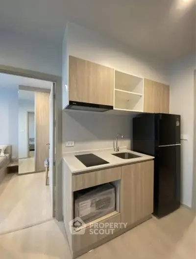 Modern compact kitchen with sleek cabinetry and black refrigerator in cozy apartment.