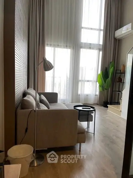 Modern living room with high ceilings and large windows offering city views.