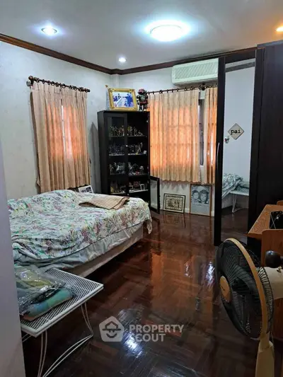 Cozy bedroom with wooden flooring, large windows, and air conditioning, perfect for comfortable living.