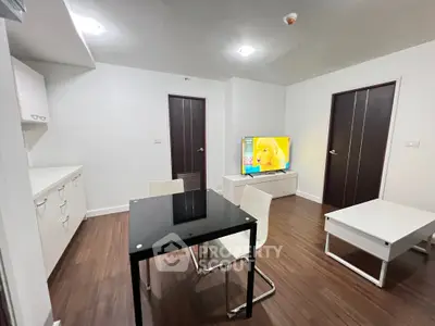 Modern living room with sleek furniture and TV, featuring wooden flooring and white walls.