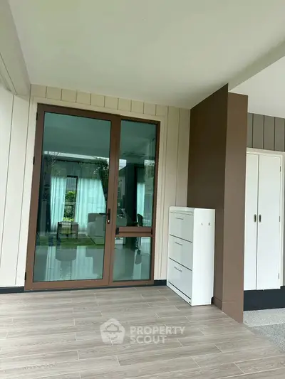 Modern patio with sliding glass door and stylish flooring, leading to a lush garden view.