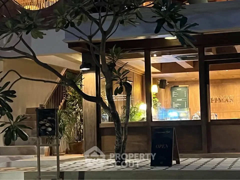 Charming entrance of a modern building with warm lighting and lush greenery.
