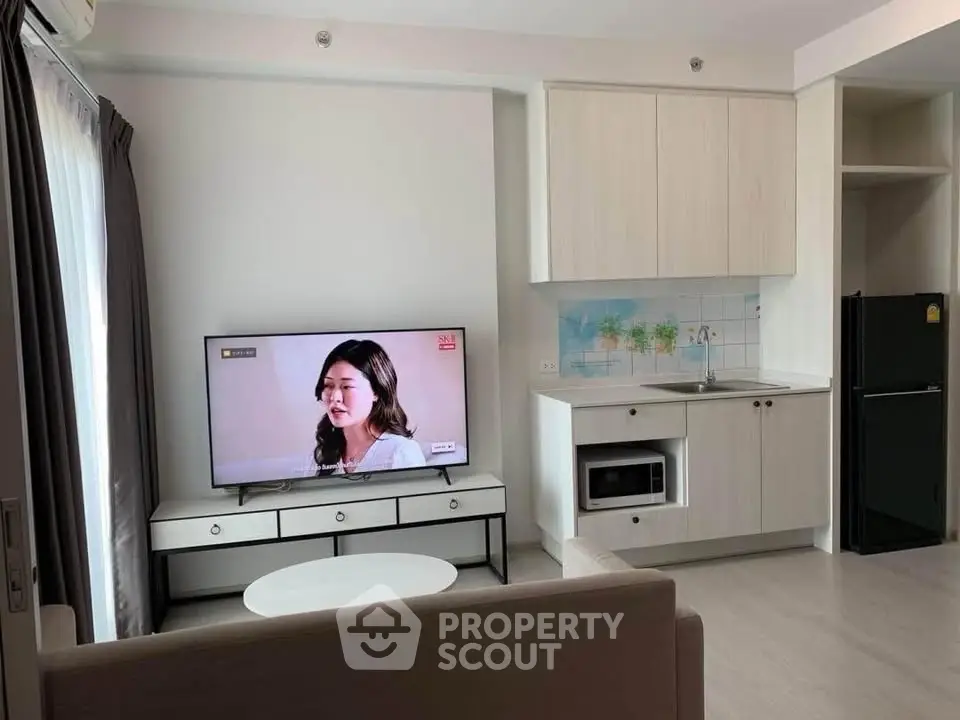 Modern living room with TV and compact kitchen in open layout apartment.