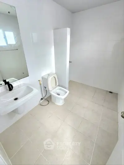 Spacious white-tiled bathroom with modern fixtures and natural light