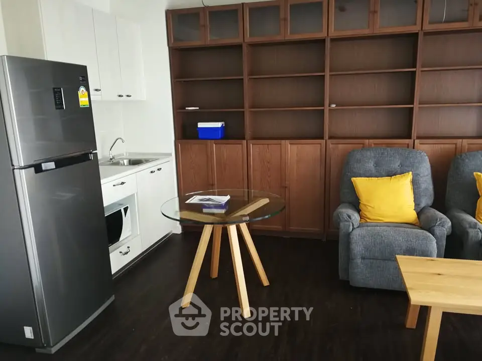 Cozy living room with modern kitchen, featuring a fridge, oven, and stylish furniture.