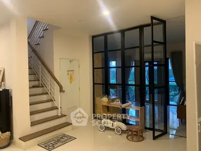 Stylish modern living room with glass partition and staircase, perfect for family gatherings.