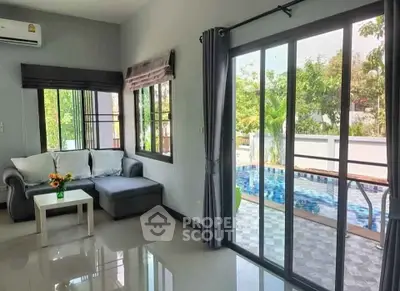 Bright living room with pool view through sliding glass doors, modern furniture, and lush greenery outside.