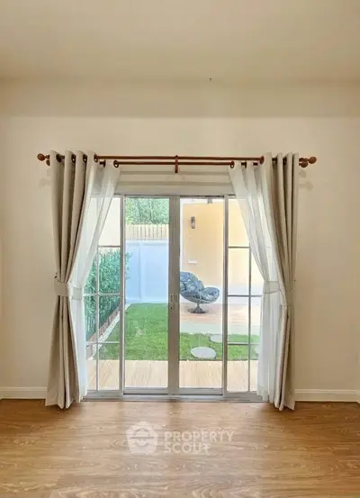 Bright living room with sliding glass doors opening to a cozy garden patio, featuring elegant curtains and wooden flooring.