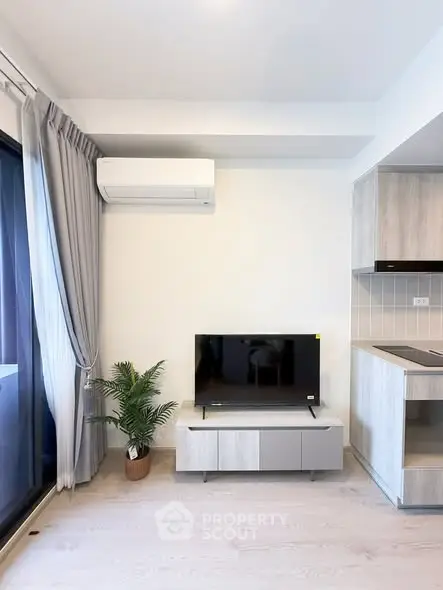 Modern living room with sleek TV setup and stylish kitchen corner in a bright apartment.
