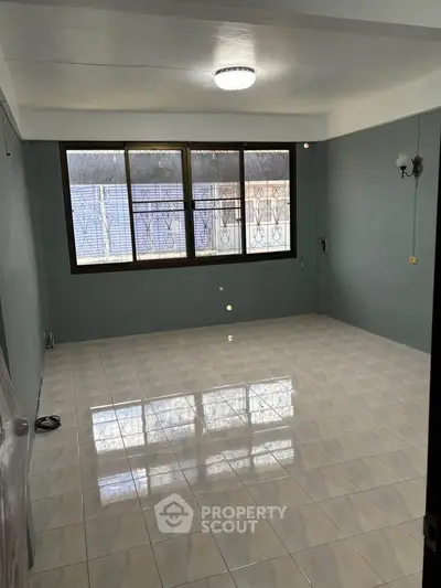 Spacious empty room with large window and tiled floor, perfect for customization.